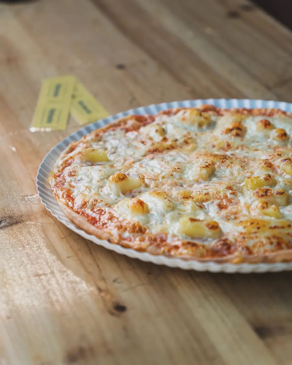 Pizza auf dem Holztisch, daneben zwei gelbe Pizza-Coupons