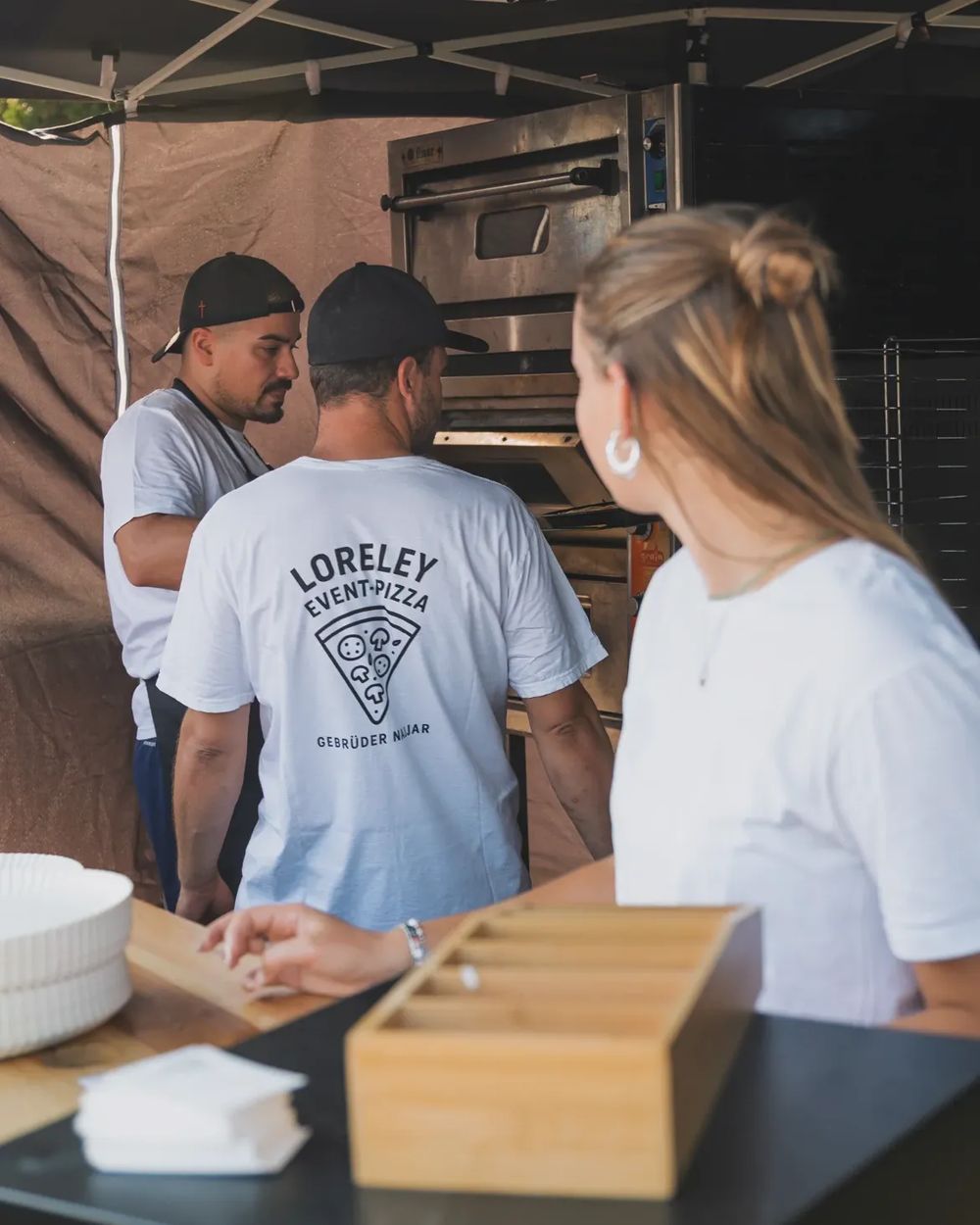 Das Team von Loreley Event-Pizza am Ofen, auf dem T-Shirt das Logo mit Pizzastück